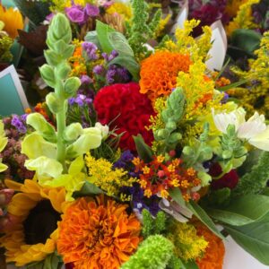 A vibrant, early fall bouquet filled with colorful flowers, including bright orange marigolds, red celosia, yellow snapdragons, and sprigs of greenery. The arrangement showcases rich hues of red, yellow, orange, and purple, creating a lively and seasonal display.