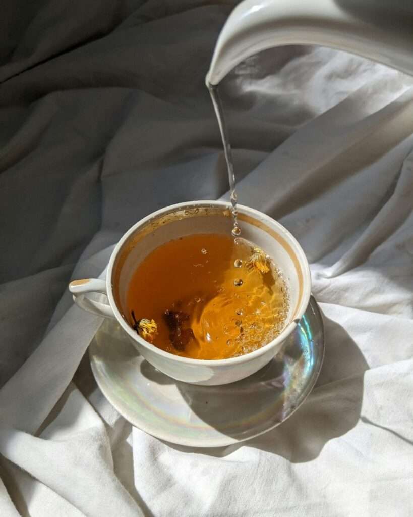Hot water being poured into a white teacup filled with golden tea, creating a calming daily tea ritual.